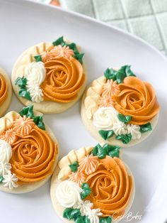 four decorated cookies on a white plate with green leaves and orange icing, arranged in the shape of flowers