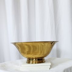 a golden bowl sitting on top of a white table cloth next to a stack of books