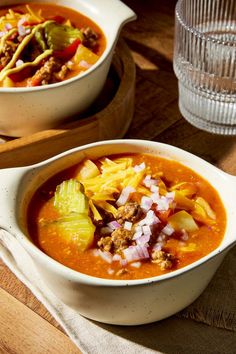 two bowls of chili soup on a wooden table with a glass of water in the background