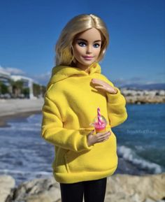 a barbie doll wearing a yellow sweater and black leggings holding a cupcake