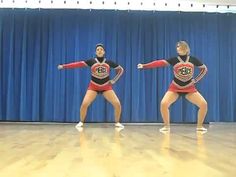 two women in red and black cheerleader outfits are dancing on a wooden floor with blue curtains behind them