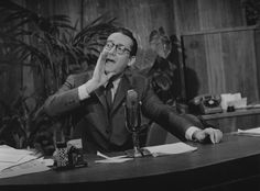 an old black and white photo of a man sitting at a desk in front of a microphone