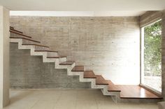 an empty room with concrete walls and wooden steps leading up to the second floor window