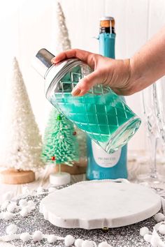 a person is pouring green liquid into a glass bottle on top of a snow covered table