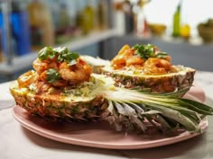 two pineapple halves with shrimp on them sitting on a pink plate in front of a bar