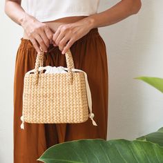 This handmade straw handbag is crafted from organic water grass hyacinth in Thailand by Thai women artisans. We designed a minimalist drawstring closure at the top to add a relaxed touch to this handbag. Ensure the safety of your belongings with our durable woven bag featuring a 100% natural dyed cotton inner lining, and a small pocket inside for your essentials, complemented by a ribbon closure adorned with unique pearl beads. It is more than just a handbag, it symbolises elegance and relaxation. Spring Rectangular Braided Bags, Spring Braided Rectangular Bag, Spring Braided Rectangular Bags, Elegant White Straw Bag With Bamboo Handle, White Handheld Straw Bag With Braided Handles, Natural Shoulder Bag With Pearl Handle For Everyday, Summer Bags With Pearl Handle In Natural Color, Summer Square Bag With Pearl Handle, Natural Bags With Pearl Handle For Summer