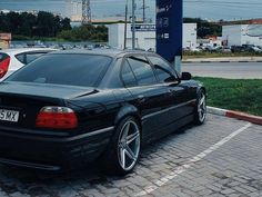 a black car parked in a parking lot next to a blue gas station sign and some cars