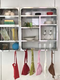 several purses hanging on the wall in front of a shelf with dishes and utensils