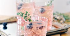 three glasses filled with pink liquid sitting on top of a wooden table next to a tray