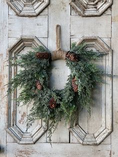 a wreath with pine cones and greenery hanging on a door