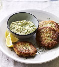 two crab cakes on a white plate with a bowl of dip and lemon wedges