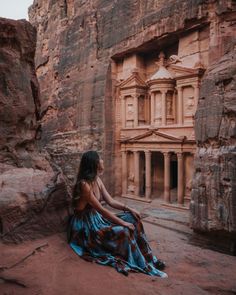 a woman sitting on the ground in front of a cliff side building with carved carvings