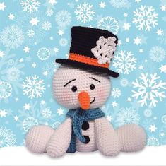 a crocheted snowman with a hat and scarf sitting in front of snowflakes