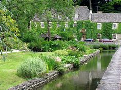 a river running through a lush green park next to a tall building with windows on it