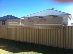 a tan fence in front of a house with grass on the ground and two houses behind it