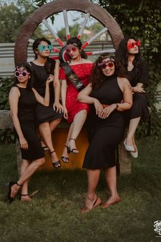 four women in black dresses and sun glasses posing for a photo with a wheel behind them