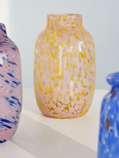 three different colored vases sitting next to each other on a white counter top with blue and yellow speckles