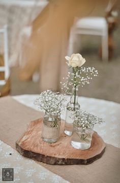 two vases with baby's breath flowers are sitting on a wood slice at an outdoor table