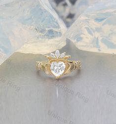 a gold ring with a heart shaped diamond in the center and leaves on each side