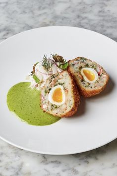 two pieces of bread with an egg in the center on a white plate next to a green sauce