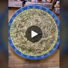 a blue and yellow plate filled with pasta on top of a wooden table next to other items