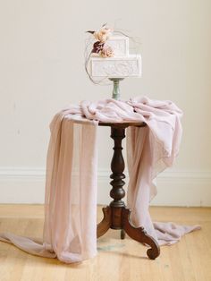 a small table with a pink blanket on it and a flower in a vase next to it