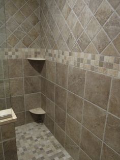 a walk in shower sitting next to a tiled wall and floor covered in brown tiles