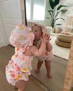 a baby standing in front of a mirror with its hands on her face and looking into the mirror