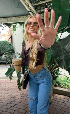 a woman with her hand up in the air while wearing jeans and holding a coffee cup