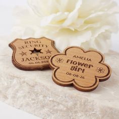 two personalized wooden flower girl tags on a white marble slab next to a white flower