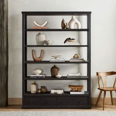 a black shelf with vases and other items on it next to a wooden chair