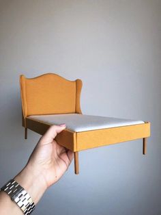 a person holding up a miniature bed with no sheets on it's headboard