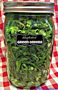 a jar filled with green onions on top of a red and white checkered table cloth