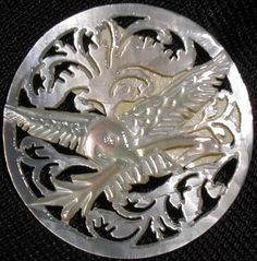 a silver plate with a bird and flowers on it's side, sitting on a black surface