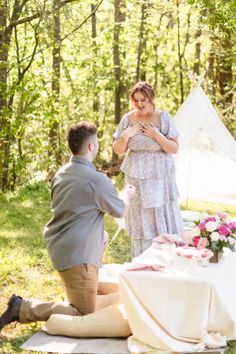 a man kneeling down next to a woman in front of a table with flowers on it