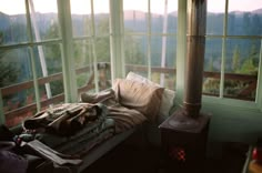 an unmade bed sitting in front of two windows with mountains out the window behind it