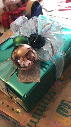 a present wrapped in green wrapping paper with a bow on top and a christmas ornament