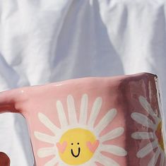 a hand holding a pink coffee mug with a smiley face painted on it