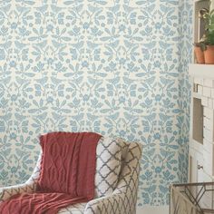 a chair with a blanket on it in front of a wallpapered fireplace and potted plant