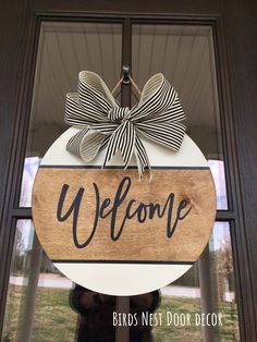 a welcome sign hanging from the side of a building with a bow on it's front door