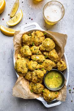 a white bowl filled with fried food next to lemon wedges