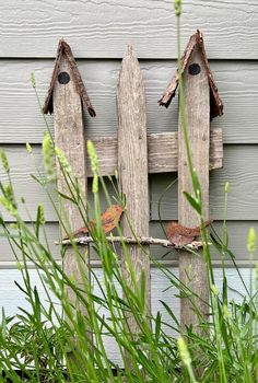 two wooden birdhouses on a fence in front of a house with grass growing around them