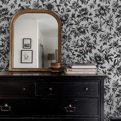 a dresser with a mirror on top of it next to a wallpapered wall