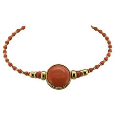 This marvelous 1980 circa Italian necklace is of chic design and beautifully made A large centerpiece of 3 cm. including the gold frame made of the finest flawless quality natural Coral cabochon beautifully polished to perfection, fascinating color, measuring 27.8 mm diameter, nestled into a gold frame circle makes the focal point of this unique necklace With graduated beads of gold and coral set on a gold torque adorning the neckline Chic and unique, looks beautiful when worn Fine condition throughout Further Details Below Metal: 18 Kt yellow gold Hallmarks: Italian assay and maker Gems: 1 round cabochon cut natural coral of 27.8 mm in diameter – 2 natural coral beads of 8.5 mm in diameter - 32 natural coral beads of 4.9 mm. in diameter Measures: length is 40 cm – centre medallion is 3 cm