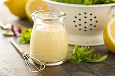 a glass jar filled with dressing next to lemons and parsley