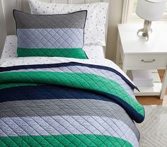 a bed with a green, blue and grey quilted coverlet on top of it