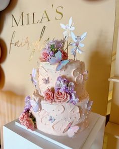 a three tiered cake with pink frosting and flowers on top, sitting on a white box