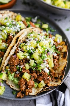 two tacos filled with meat and vegetables on a plate next to bowls of salsa