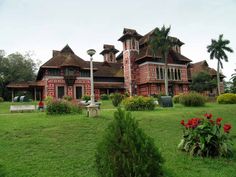 a large red and white building sitting in the middle of a lush green field next to flowers