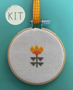 a cross stitch kit with a flower on it and a yellow ribbon hanging from the hoop